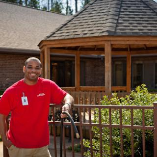 A person standing by a wooden fence, smiling in front of a gazebo.