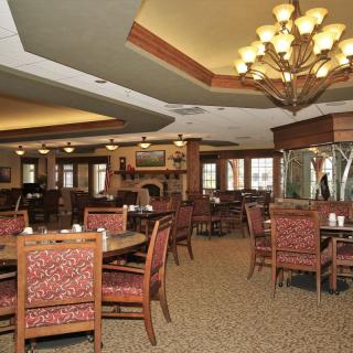 A spacious and elegantly designed dining room with multiple tables and chairs arranged under a large chandelier.