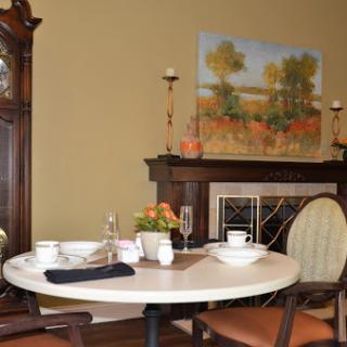 A cozy dining area featuring a round table set for a meal, complemented by an artwork hanging above the fireplace.