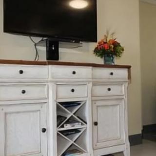 A living room setup featuring a mounted TV above a white cabinet with various drawers and shelves, adorned with a bouquet of flowers.