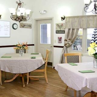 A cozy dining room with neatly arranged tables and chairs, adorned with flowers and elegant lighting.