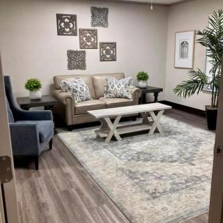 A cozy living room featuring a sofa, armchair, and coffee table with decorative artwork and plants.