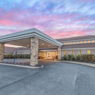 A building with a covered entrance and driveway, set against a colorful sunset sky.