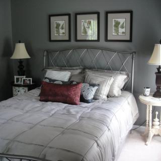A cozy bedroom with a neatly made bed, decorated with pillows and flanked by two lamps on nightstands. Three framed artworks adorn the wall above the headboard.
