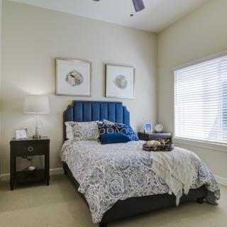 A modern bedroom with a blue upholstered headboard, decorative pillows, and framed artwork on the walls.