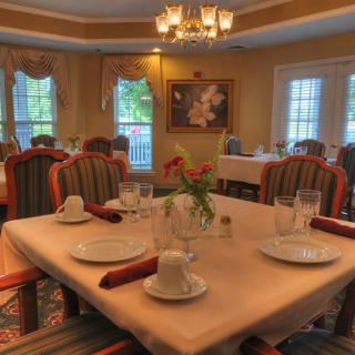 An elegant dining room with a neatly set table, featuring soft lighting and a chandelier.