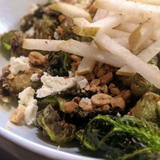 A delicious salad featuring roasted Brussels sprouts, topped with feta cheese, crunchy nuts, and fresh pear slices.