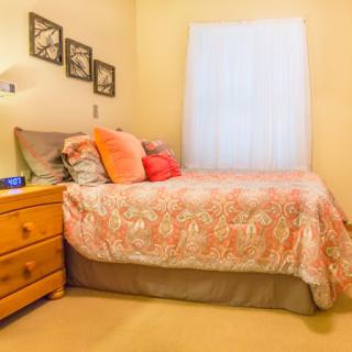 A cozy bedroom with a neatly made bed, pillows, wooden dresser, and decorative wall art.