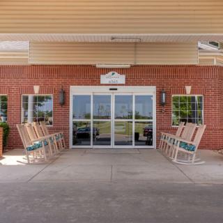 Entrance of a building with rocking chairs lined up along the brick wall.