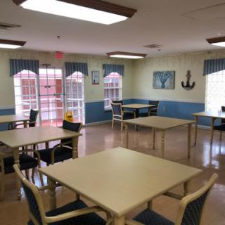 A spacious dining area decorated in a coastal theme, featuring several tables and chairs, with large windows allowing natural light.