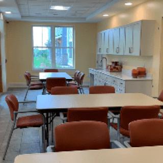 A neatly arranged dining area with tables, chairs, and a kitchenette.
