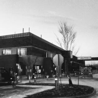 A monochrome view of a modern building surrounded by a landscaped area at dusk.