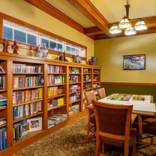 A cozy library room with wooden bookshelves filled with books and a central table surrounded by chairs.