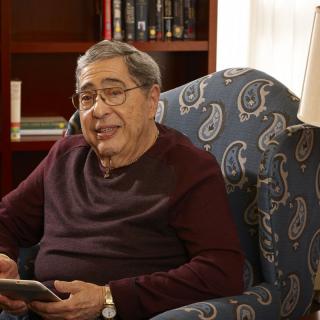 An older man sitting in an armchair with a book in his hand.
