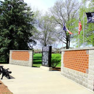 A serene memorial park featuring flags and brick walls, surrounded by lush greenery.