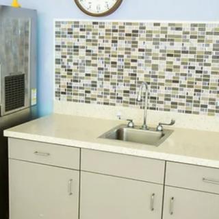 A small kitchen area with a tiled backsplash and a stainless steel sink on a white countertop.