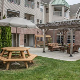 A cozy outdoor patio area with picnic tables and seating under a pergola, set in an apartment complex.