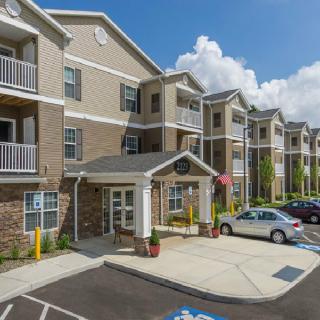 A modern apartment building with a parking lot, featuring a central entrance and surrounded by clear skies.