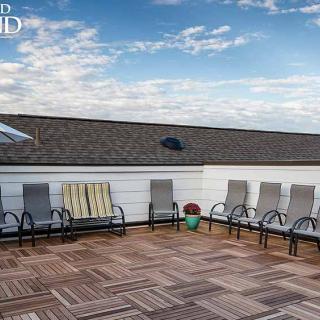A rooftop patio with several chairs arranged on a wooden deck under a blue sky with clouds.