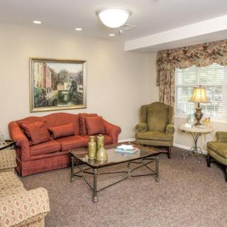 A cozy living room with a red couch, two green armchairs, and a glass coffee table.