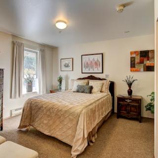 A cozy bedroom featuring a neatly made bed, tasteful artwork, and warm natural light.