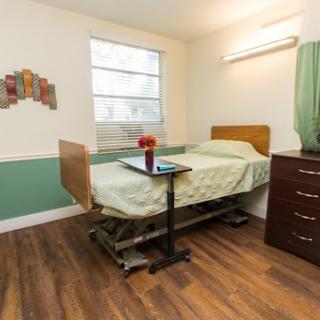 A well-lit hospital room featuring a bed, a small table with flowers, and a nightstand.