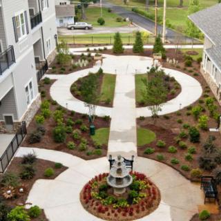 A beautifully designed courtyard with a symmetrical pathway, surrounded by lush greenery and a central fountain.