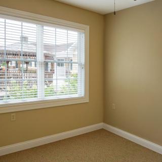 A bright empty room with beige walls and a large window letting in natural light.