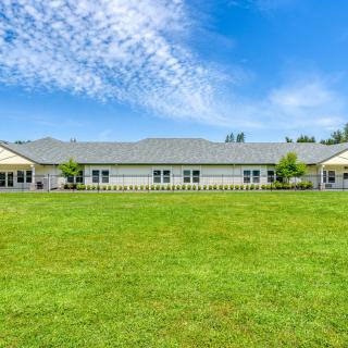 A wide one-story residential building with a large green lawn under a blue sky.