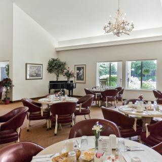 A spacious dining room with elegantly set tables and a chandelier, overlooking a scenic view through large windows.
