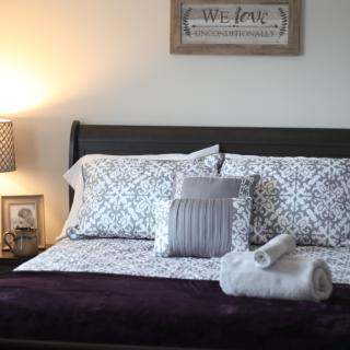 A neatly made bed with patterned bedding and decorative pillows, accompanied by rolled towels and a lit lamp on the side.