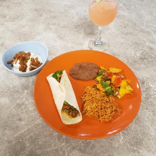 A colorful Mexican meal featuring a taco, rice, vegetables, refried beans on an orange plate, accompanied by a dessert and a refreshing beverage.