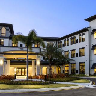 A beautiful residential building with well-maintained landscaping and palm trees, seen in the evening light.