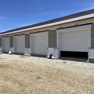 A row of newly constructed storage unit garages with closed doors under a clear blue sky.
