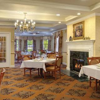 A cozy and elegant dining room with beautifully set tables, a chandelier, and a warm fireplace.