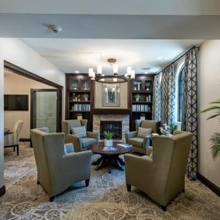 A cozy living room with armchairs arranged around a small table, featuring bookshelves and a chandelier.