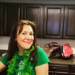 A woman smiling in a kitchen, wearing a green shirt.