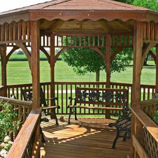 A beautifully crafted wooden gazebo with benches, surrounded by a lush green landscape.