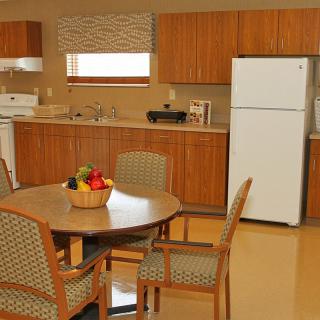 A cozy kitchen with a dining table set for four, featuring wooden cabinets and a fruit basket on the table.