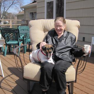 A woman sitting on a deck chair with a dog on her lap enjoying a sunny day.