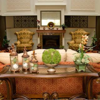 A classic-style living room with elegant furniture, featuring a sofa, armchairs, and a fireplace, adorned with decorative plants.