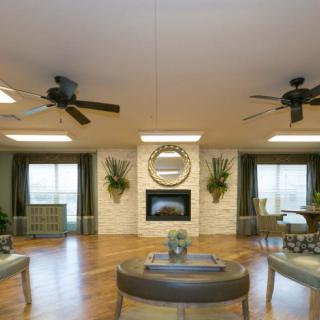 A spacious living room with elegant decor, featuring a central fireplace, ceiling fans, and ample seating.