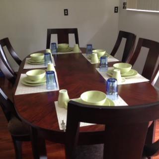 A neatly set dining table with green plates and blue glasses, surrounded by wooden chairs.