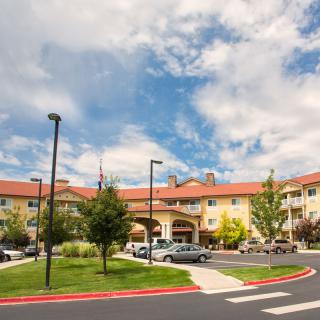A sunny day view of a large building with a parking lot and landscaped grounds.