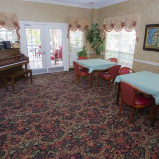 A comfortable room with tables, chairs, a piano, and large windows.