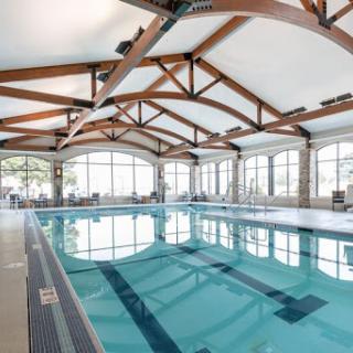 A spacious indoor swimming pool featuring elegant wooden beams and large windows, allowing for plenty of natural light.