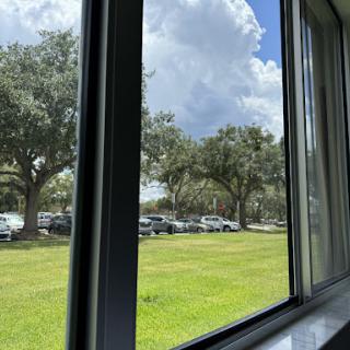 A view from a window showcasing a grassy area with trees and parked cars under a partly cloudy sky.