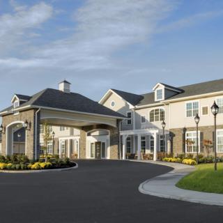 A large residential building with a covered entrance and landscaped surroundings under a clear blue sky.