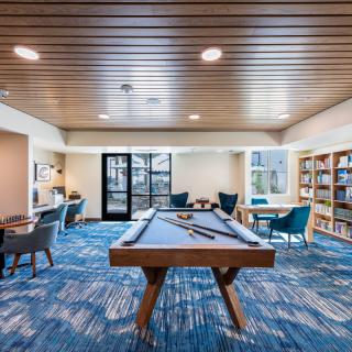 A modern recreation room featuring a pool table, bookshelves, and a comfortable seating area.