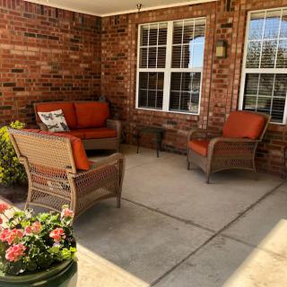 A cozy patio with wicker furniture and bright orange cushions, accented by potted plants and surrounded by brick walls.